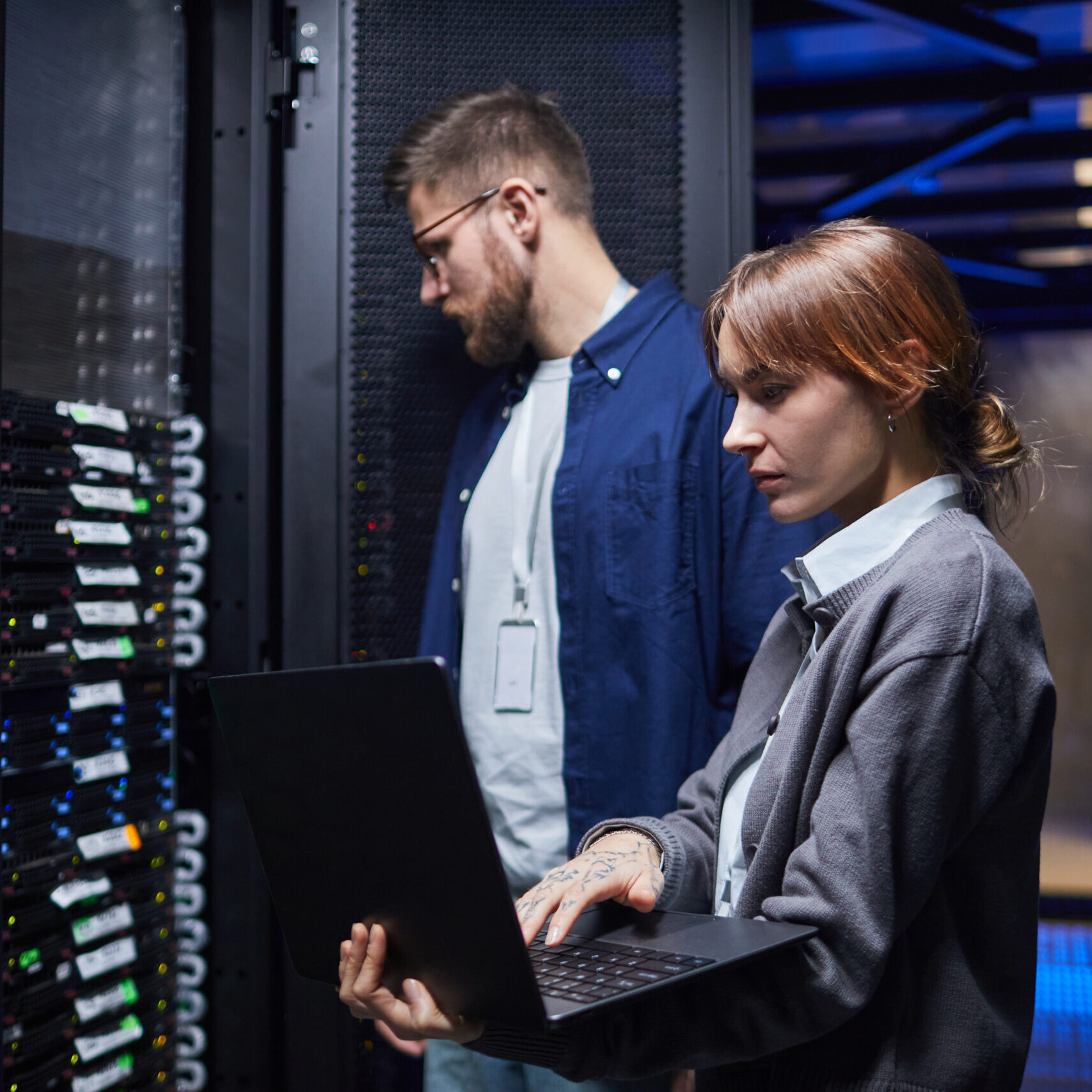 IT professionals in a data center managing server operations while collaborating on tasks with laptops. Focused on server health and data management