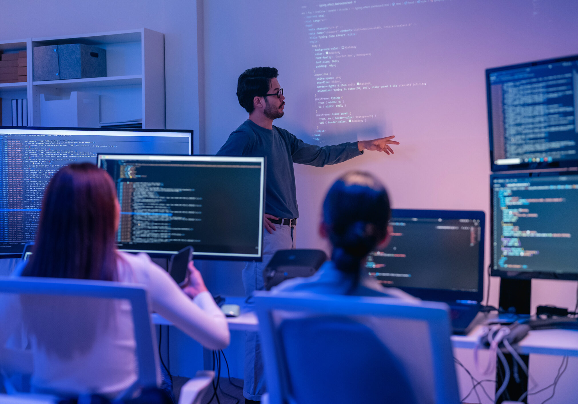 young Asian software development manager leads a late-night office discussion with his executive team, mentoring developers and analyzing source code to guide programming and project development